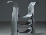 une sculpture métallique abstraite dans une pièce sombre, sur fond gris