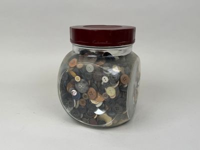 un bocal en verre contenant des boutons, posé sur une surface blanche