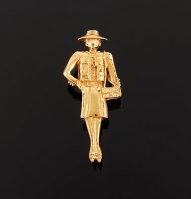 a gold plated pin with a woman in a hat and dress