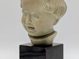 un gros plan sur une sculpture représentant la tête d'un enfant posée sur un socle noir