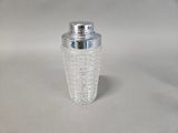 a glass shaker with a silver lid on a white surface
