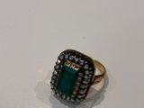 a close up of a ring with a green stone surrounded by small diamonds