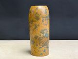 un vase jaune posé sur une table, sur fond noir