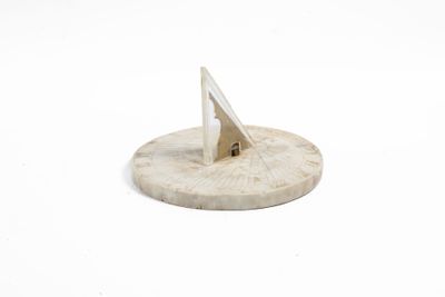 un cadran solaire en bois posé sur une surface blanche, avec un fond blanc