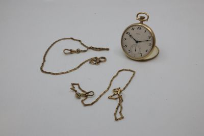 a small gold pocket watch and chain on a white surface