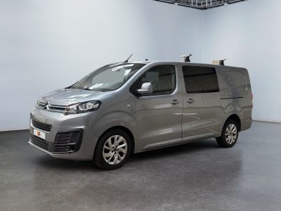 La camionnette argentée est garée dans une grande pièce aux murs blancs.