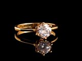 un gros plan d'une bague en or sertie d'un diamant, posée sur une surface noire