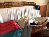 a wicker bed in the corner of a room with clothes on the floor