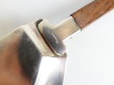 une grande spatule en métal avec un manche en bois posée sur une surface blanche