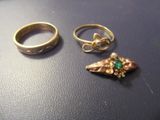 two gold rings and a ring with a green stone on top of a table