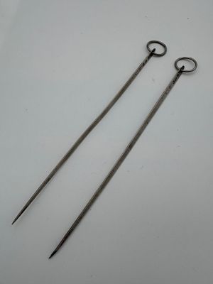 pair of long metal scissors on a white surface with a white background