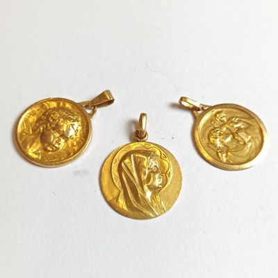 un gros plan sur trois pendentifs en forme de pièces d'or posés sur une surface blanche