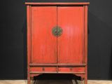 une vieille armoire rouge posée sur un parquet, près d'un mur noir