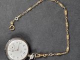a silver pocket watch on a chain on a table