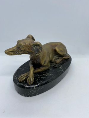 statue of a dog laying on a black base on a white surface