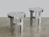 une paire de tabourets en acier inoxydable posés sur un sol en béton, avec un mur blanc en arrière-plan