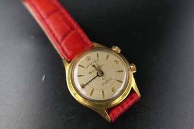 a gold watch with a red strap on a black surface