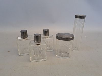 quatre petits bocaux en verre munis de couvercles argentés sont alignés sur une surface blanche