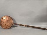 an antique copper strainer with a wooden handle on a white background