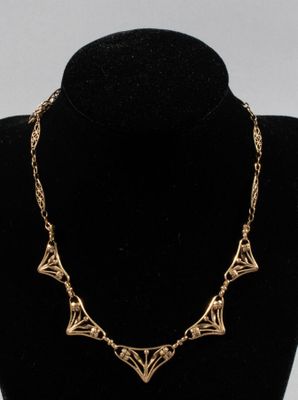 a gold necklace on a mannequin neck with a black background