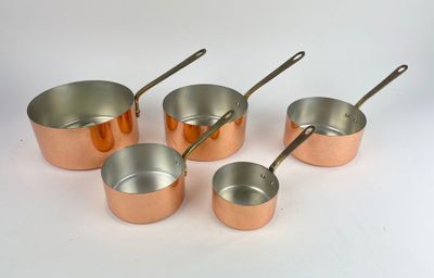 six casseroles et cuillères en cuivre sont alignées sur une surface blanche