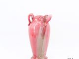 un vase rose à deux anses posé sur une surface blanche