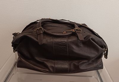 un sac de voyage en cuir posé sur une chaise en plastique transparent
