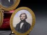 trois portraits miniatures d'un homme et d'une femme posés sur un coussin de velours rouge