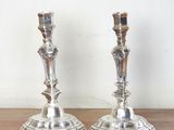une paire de bougeoirs en argent posés sur une table en bois devant un mur blanc