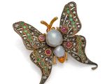 un gros plan sur une broche en forme de papillon ornée de perles et de pierres précieuses