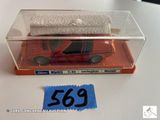 une voiture rouge dans une boîte transparente, sur laquelle est accrochée une étiquette bleue