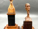 pair of wooden busts of two men with a plaque in the middle of them