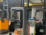 Plusieurs chariots élévateurs sont garés dans un grand entrepôt où se trouvent des panneaux jaunes et noirs