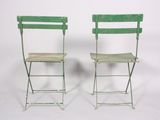 pair of green metal folding chairs against a white backdrop