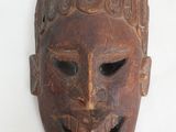 un vieux masque en bois accroché à un mur blanc