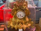 a gold clock under a glass clochet on a table