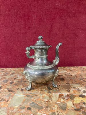 silver plated teapot on marble table with red wall in background