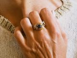 the woman is wearing a gold ring with a blue stone on it