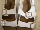white leather sandals with buckles on the toes on a wooden floor