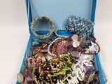 a blue box filled with assorted jewelry on a white surface