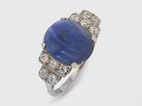 un gros plan d'une bague en pierre bleue et diamants posée sur une surface blanche