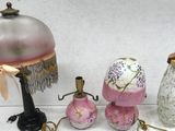 une table sur laquelle se trouvent une lampe, un abat-jour, un vase et d'autres objets