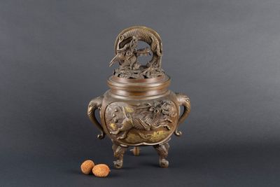 un vase en bronze orné d'un oiseau, avec une noix posée à ses pieds