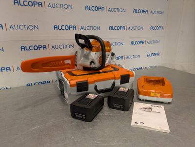 une tronçonneuse orange et noire posée sur une table, à côté d'un chargeur
