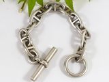 silver chain bracelet with a cross charm on a white surface next to a green plant