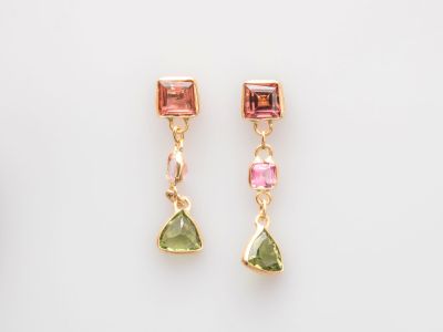 une paire de boucles d'oreilles en tourmaline rose et verte posées sur un fond blanc