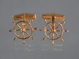 two pairs of gold cufflinks with a ship wheel on them