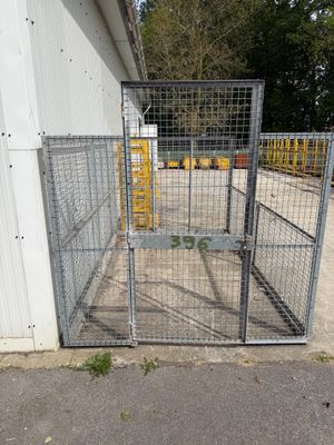 une grande cage métallique munie d'un portillon, située devant un bâtiment