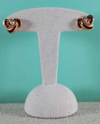 une paire de boucles d'oreilles rouges et dorées posées sur un présentoir blanc
