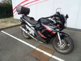 une moto noire garée sur un parking, près d'un mur blanc